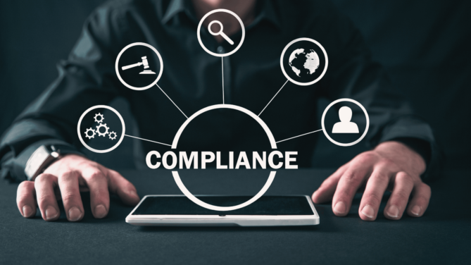 Professional man sitting at a table with a tablet, the word "compliance" floats above it with icons that are a part of it.